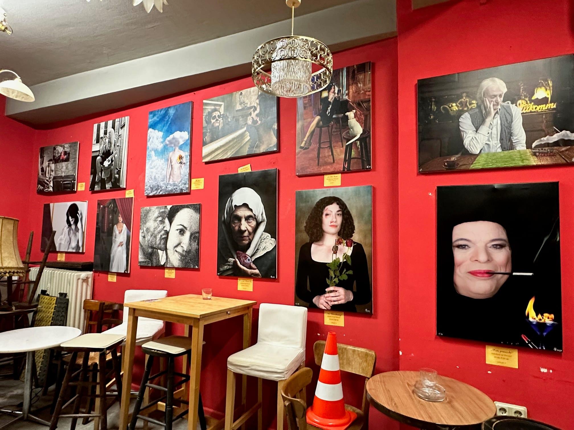Ausstellungswand im Kunst- und Kulturclub Die Winzer: gerahmte Fotoarbeiten mit Beschriftung auf roter Wand
